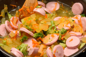 Close-up of cooking vegetable stew with sliced sausages.