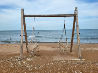 Broken wooden swing on a sandy beach near the sea.