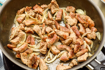 Fragrant meat is fried with onions in a frying pan.