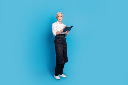 Full size photo of retired female write order notebook barista small coffee shop owner wear waitress uniform isolated on blue background