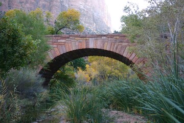 photo of arched block bridge on zion park with red bluffs background and green grassy foreground