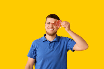 Young man with piece of tasty pepperoni pizza on yellow background