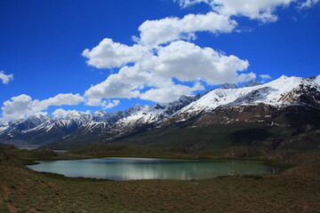 Clouds over the snow covered peaks and an alpine lake