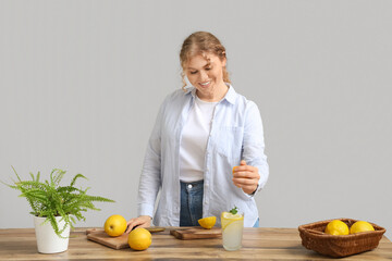 Young woman squeezing lemon juice into glass of water at home