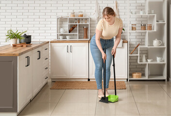 Young woman sweeping floor in kitchen
