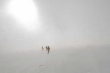 A strong terrible blizzard in the mountains and a group of tourists walking into the distance into...