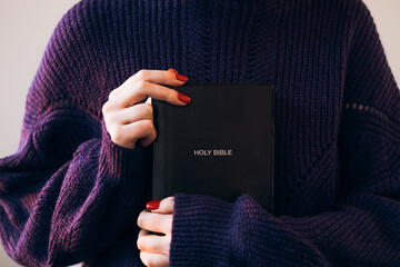Christian woman in cozy sweater, holds holy Bible in hands.