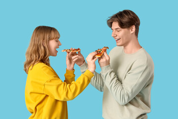 Beautiful young couple feeding each other tasty pizza on blue background
