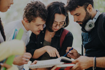 A multicultural group of students collaborate on school tasks in a park, showcasing teamwork and learning. The setting is relaxed, emphasizing education and connection among young adults.