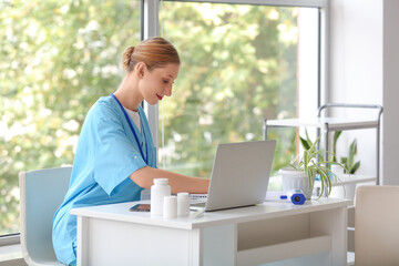 Happy female doctor working with laptop near window in clinic