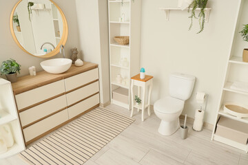 Modern toilet bowl, chest of drawers with sink and mirror near white wall in restroom