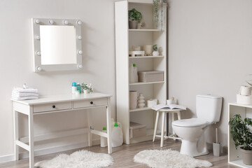 Modern toilet bowl, shelving unit and table with mirror near grey wall in restroom