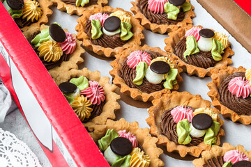 Set of mini basket cakes or sand tartlets cake with cream in box on light background with flowers and cup of tea. Sweets, dessert and pastry, close up