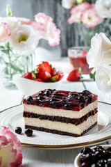 Piece of delicious mousse cake with berry jelly on plate over grey background with cup of juice, berries and flowers. Holiday sweets, dessert and pastry, close up