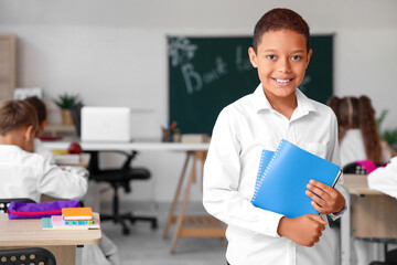 Little African-American schoolboy with notebooks in classroom