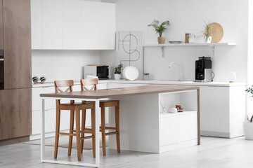 Interior of light kitchen with modern island table and white counters