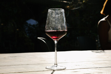glass of red wine filled to the brim, sitting on a table indoors. The glass has a slender stem and a broad bowl, showcasing the rich red color of the wine