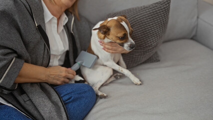 A woman grooming her dog indoors on a comfortable sofa, showcasing a tender moment between a pet and its owner in a cozy living room setting.