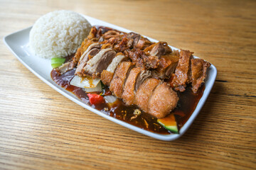 Crispy roasted duck slices on vegetables with sauce and rice served on a white square plate on a wooden table in a Chinese restaurant, copy space, selected focus