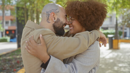 Fototapeta premium Interracial couple embracing lovingly in a sunny urban park, depicting joy and diversity.