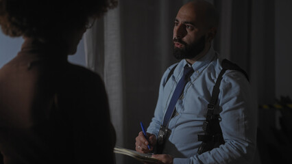 Man interviews silhouette of a woman in a dimly lit interrogation room, badge visible