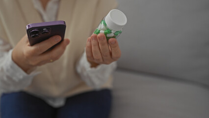 A middle-aged woman indoors, holding a bottle of pills and smartphone, possibly searching for medication information.