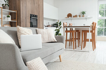 Interior of light kitchen with counters and laptop on sofa