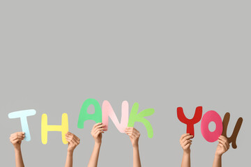 Female hands holding text THANK YOU made of paper on grey background