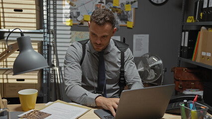 Handsome hispanic man working on laptop in a detective office setup with evidence board.