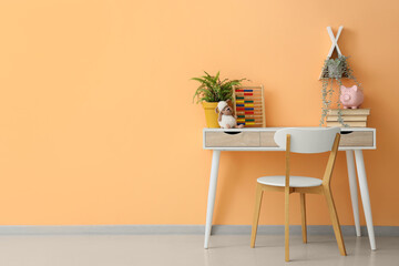 Table with books, abacus and plants near orange wall in children's room