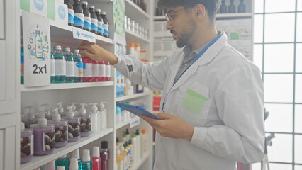 Handsome arab pharmacist with beard organizes medicine shelves in a modern drugstore while holding a tablet.