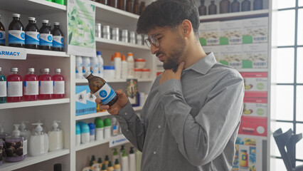 A young man examines a medicine bottle inside a well-stocked pharmacy, contemplating its label carefully.