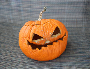 Wrinkled carved pumpkin with a spooky expression on a fabric background.