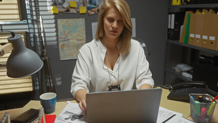 A focused blonde woman working on a laptop in a cluttered detective office, surrounded by files and...