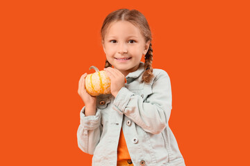 Cute little happy girl in autumn clothes with pumpkin on orange background