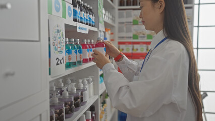 A young asian woman pharmacist examines products on shelves in a modern pharmacy interior.