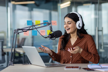 Latin American woman businesswoman recording podcast with microphone and laptop, wearing...