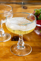 Pouring of brut champagne bubbles wine in coupe glasses and small bowl with fresh strawberries