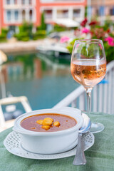 Homemade tasty fish or bisque soup with croutons served with glass of cold rose wine and view on yacht boats and houses of Port Grimaud, French Riviera, France. Food of Provence