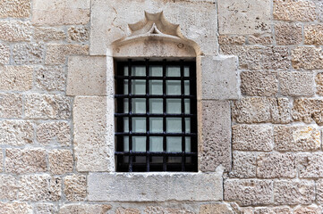 Rectangular window with black colored metal grille on an old beige colored stone wall. From the Peace window series.