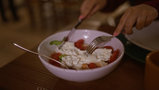 Woman dining indoors at an italian restaurant, enjoying a bowl of fresh burrata salad with tomatoes.