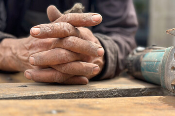 closeup of clasped rough dirty  hands of elderly hard working carpenter over wood plank 