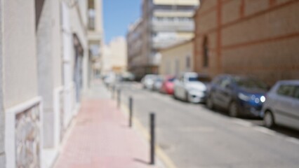 Blurred background of an outdoor street scene with defocused buildings and parked cars under a clear blue sky.