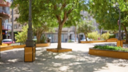 Defocused view of a sunny park with lush trees and benches, capturing a blurred urban outdoor setting with bokeh effect and soft background details.