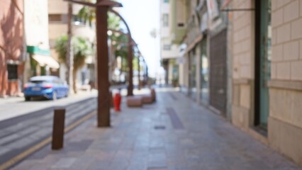 Fototapeta premium Blurry image of a quiet street with a defocused background, featuring a parked car, buildings, and trees lining the sidewalk in an outdoor urban setting