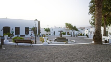 Blurred picturesque outdoor plaza in lanzarote, spain, featuring white buildings, a fountain, and palm trees with a defocused background providing a serene atmosphere
