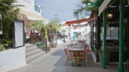 Blurred view of an outdoor cafe in lanzarote, spain with defocused palm trees and seating arrangements in a bright day, capturing the essence of a sunny canary islands street.