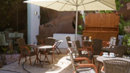 Blurred outdoor cafe in lanzarote, spain with wicker chairs, tables, large umbrella, and greenery, creating a defocused, relaxing ambiance on the canary islands