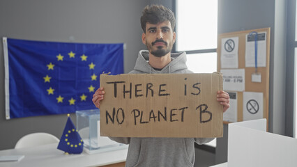 A young man holding a protest sign about environmentalism against a backdrop of an eu flag in a modern office.