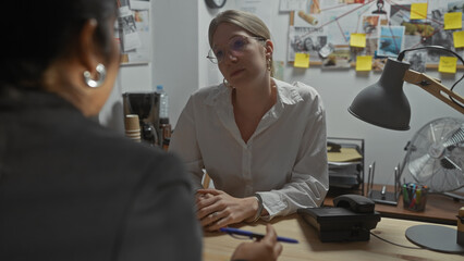 Two women engage in serious discussion in a cluttered investigation office with visible case...